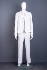 Dummy in female white blazer and trousers. Formal style costume for ladies, grey background. Feminine fashion style.