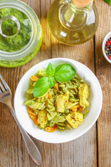 Pasta with chicken pieces and pesto sauce on an old wooden table.
