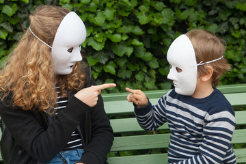 Girl and boy with a white mask pointing at each other with their finger