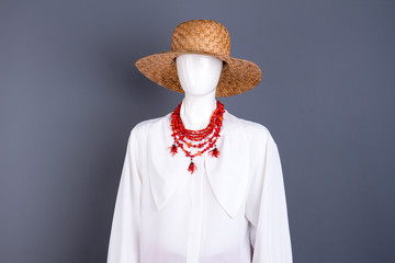 Straw hat and white elegant blouse. Female mannequin with woven hat, white shirt and red necklace, studio portrait. Feminine beauty and fashion.