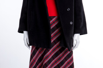 Close up black coat and patterned skirt. Mannequin in women overcoat, skirt and sweater close up, white background.