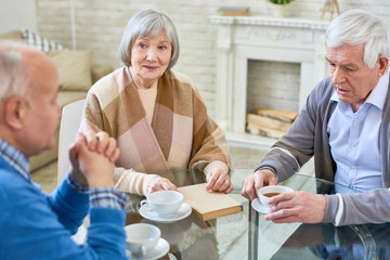 Elderly elegant woman and men having teatime at table in living room of nursing home for aged...