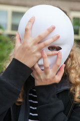 Girl with a mask with her hands covering one eye.