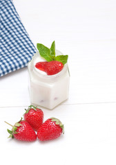 Cream with a strawberry on white wooden background.

