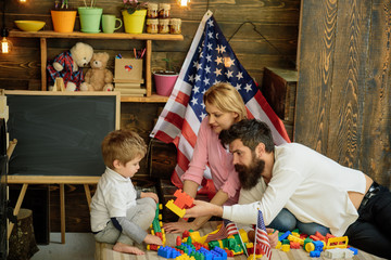 American family and cute son play with usa flags. Parents teaching son american traditions playing, enjoy parenthood. Kid with parents play with plastic blocks, flags. Patriotic education concept.