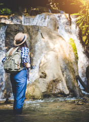 Fototapeta na wymiar Travel and freedom. Young woman in hat with rucksack enjoying tropical waterfall view.