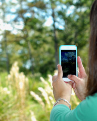 Over the shoulder shot of woman taking a pretty landscape photo of wilderness with her phone camera