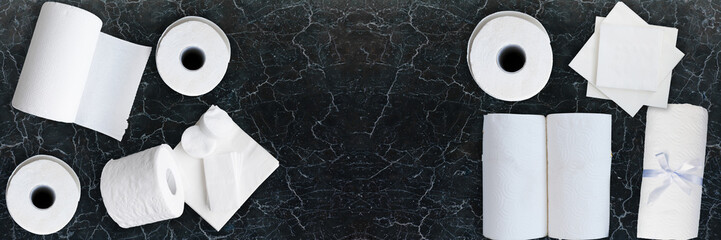Paper tissue, white toilet  paper rolls, towels, napkins, cotton pads stacked on black marble table. Top view. Copy space. Wide panoramic image.