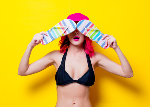 Young pink hair girl in bikini with cap and sandals. Portrait isolated on yellow background