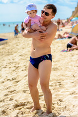 Young father in sunglasses on the beach with a little daughter