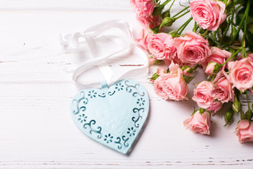 Fototapeta na wymiar Blue decorative heart and pink roses flowers on white wooden background.