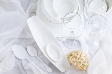 White porcelain dishes and transparent wine glasses on draped cloth. Top view. Copy space.