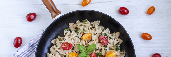 Panoramic view of cast-iron frying pan with aglio olio pasta with scattered cherry tomatoes