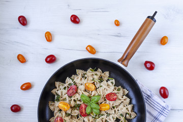 Cast-iron frying pan with aglio olio pasta with scattered cherry tomatoes