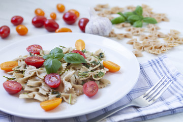 White plate with aglio olio pasta with cherry tomatoes and fresh basil