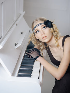Young actress with blue eyes looking up while lying on open keyboard of white piano