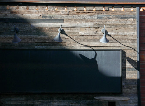 Black billboard on a wooden wall with lamps and string of lights