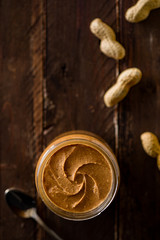 Fototapeta premium Peanut Butter in a Glass Jar with Peanuts on Wood