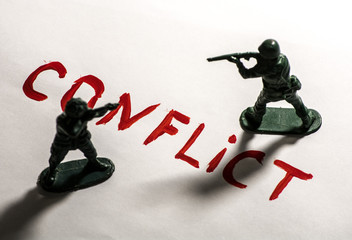 Plastic toy soldiers are on the table, on a sheet of white paper. On paper the writing " conflict."
