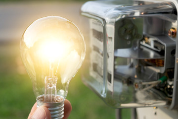 close-up hand of person holding light bulb from outdoor with watt hour meter beside
