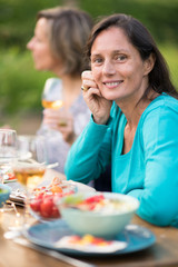 Obraz na płótnie Canvas Looking at the camera. Portrait of a beautiful brunette woman in her forties. She sits around a table in a garden with friends for dinner.