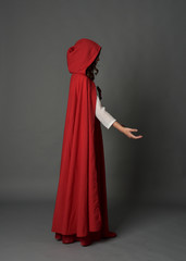 Naklejka premium full length portrait of woman wearing red fantasy costume with cloak, standing pose on grey studio background.