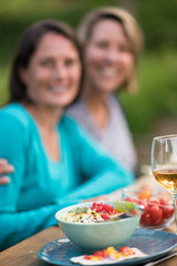 Close-up on a colorful salad in a bowl, Friends gather to share a meal around a table in the garden. Focus on the foreground