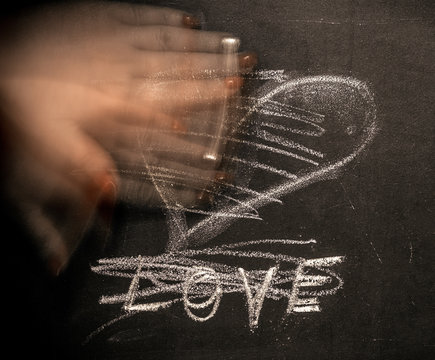 On the chalkboard written "Love" and painted heart. The female hand erases the inscription.
