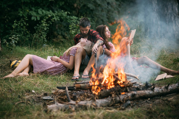 Young couple in love enjoying romantic weekend in nature. Bearded man looking at his blond girlfriend with admiration. Group of friends having picnic in woods