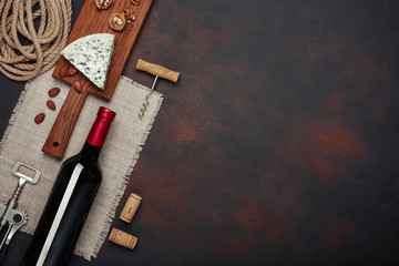 Bottle of wine, walnut, almonds, corkscrew and corks, on rusty background top view