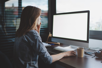 view from back to female student is talking on smartphone sitting at desk in front of monitor with blank space for design. Mockup screen with copy space. woman makes a business call