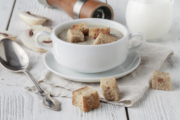 Fresh mashed mushroom soup with bread croutons and pepper on wooden background