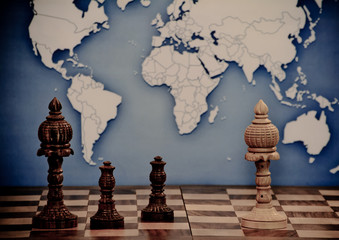 Various chess pieces are on the chessboard. Figures of two colors. In the background is a map of the world.

