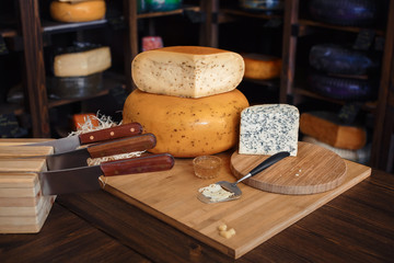 Cheese heads with slices and knives on a wooden board with an interior