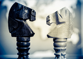 Chess pieces horse stand facing each other. In the background is a world map.
