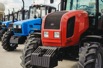 agricultural machinery, tractors stand in a row of blue and red. New working machines with square headlights