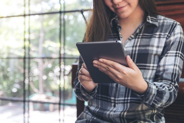 A beautiful Asian woman with smiley face holding and using tablet pc in modern cafe