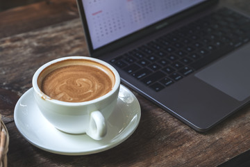 Closeup image of a cup of coffee and computer laptop on wooden table in cafe
