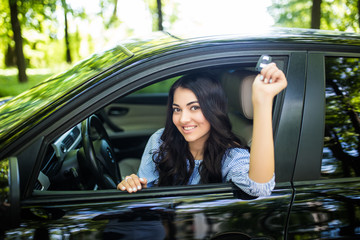 Happy female driver showing car key in her new car