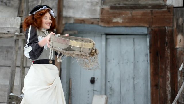 Pretty girl in a fairy-tale dress is standing by the hut and throwing snow. Fairy-tale character. Magic of miracles