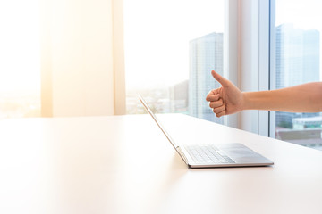 Businessman hand using laptop showing thumbs up and enjoying  when him online success, large windows outside building, city, tower view, soft focus