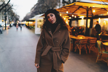 charming brunette with long curly hair walking along the pedestrian street of the European city past street cafes. Beautiful young woman is going on a date