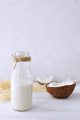 Fresh coconut milk in glass bottle with half of fresh coconut on wooden white background with place for text