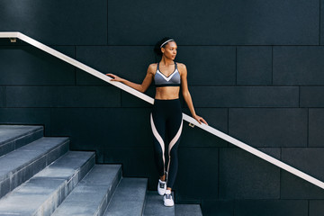 Woman in sportswear relaxing after workout, standing on staircase - obrazy, fototapety, plakaty