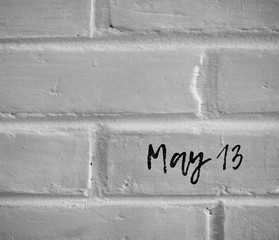 BLACK AND WHITE PHOTO OF " May 13 " WORDS WRITTEN ON WHITE PLAIN BRICK WALL