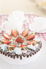 Tasty strawberry cream cake on checkered table, with tea set