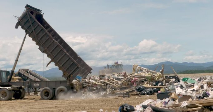 Large dump truck emptying a dumpster of construction trash at a landfill