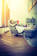 Junge Frau liegt in bequemen Ohrensessel und liest, Designerwohnung