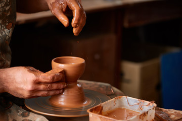 Close-up hands of a male potter in apron molds bowl from clay, selective focus