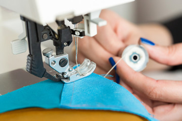 technology, manufactoring, handcraft concept. close up of the most important details in sewing machine, under thin and sharp needle there is few blue and yellow pieces of fabric